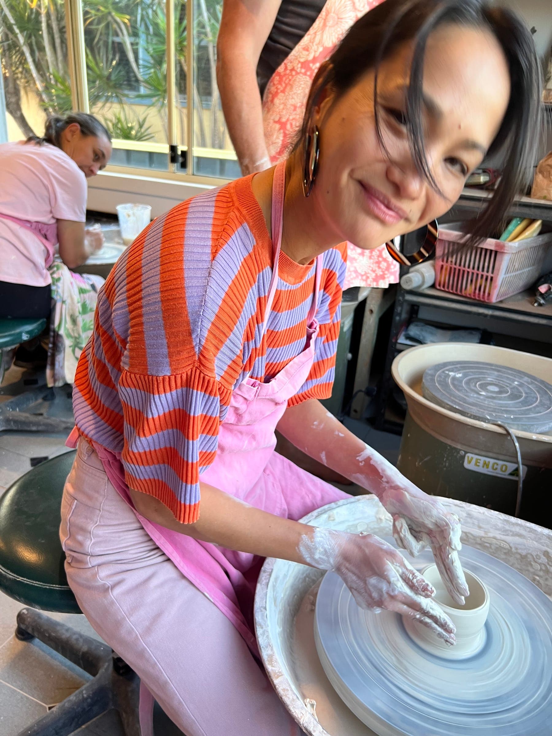 A smiling potter working at the wheel during class