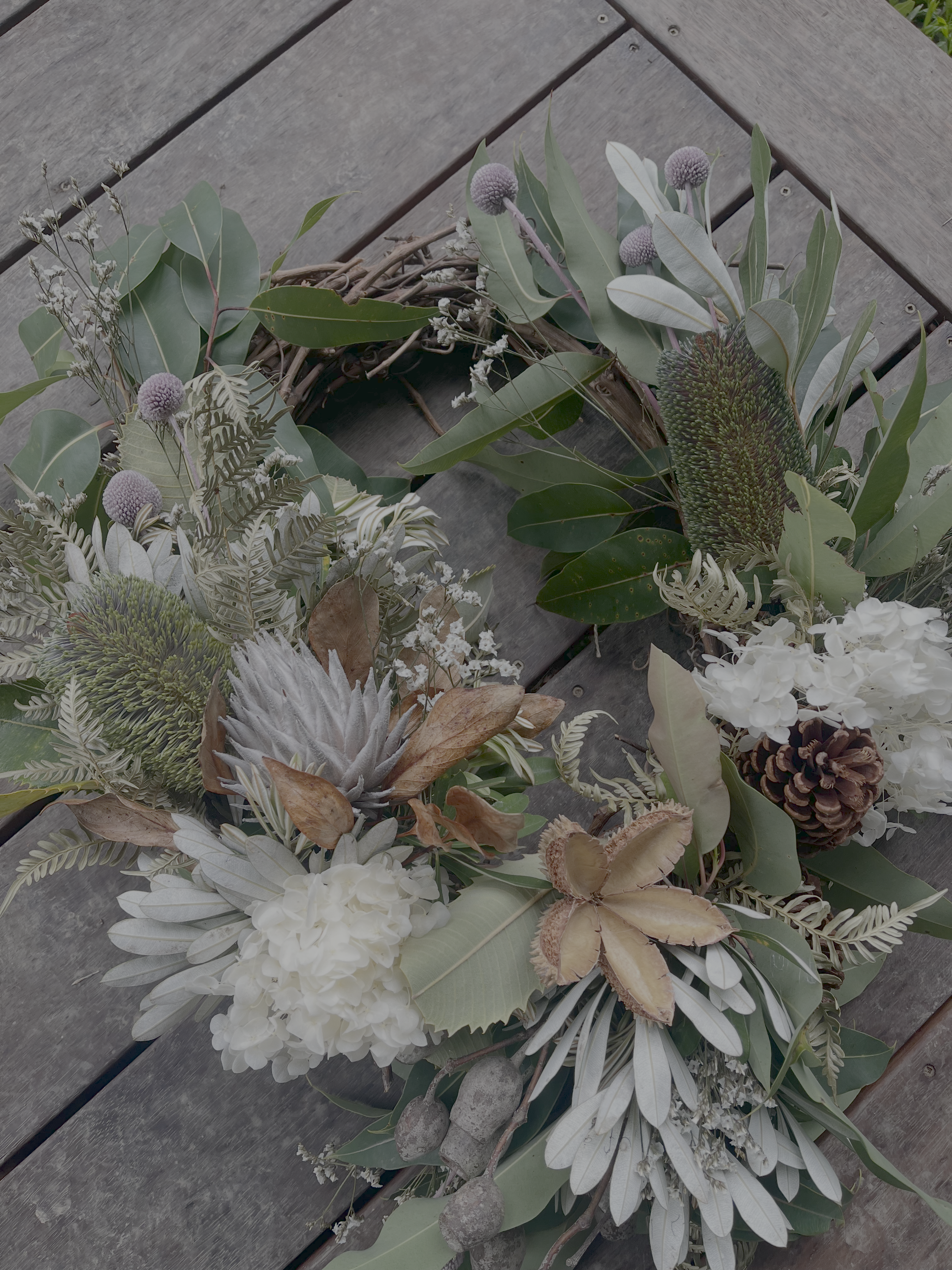 A fresh foliage Christmas wreath with white flowers and pine cones on a timber table