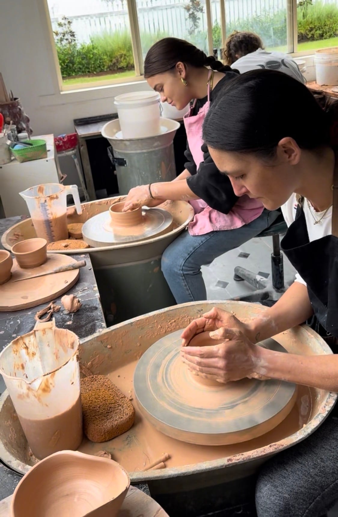 Two makers side by side at the wheel, one shaping a small bowl