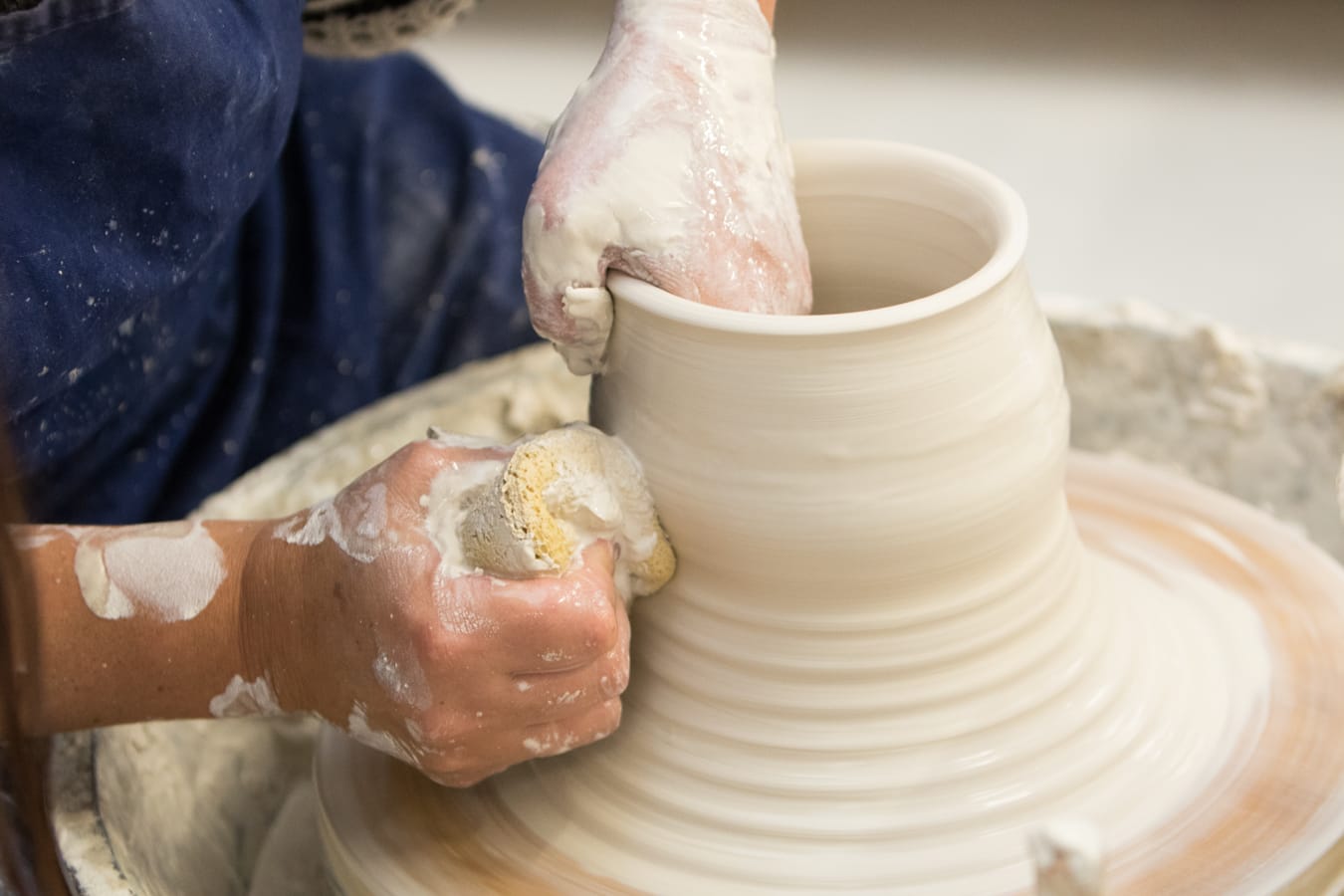 Clay covered hands pulling up the wall of a pot on the wheel