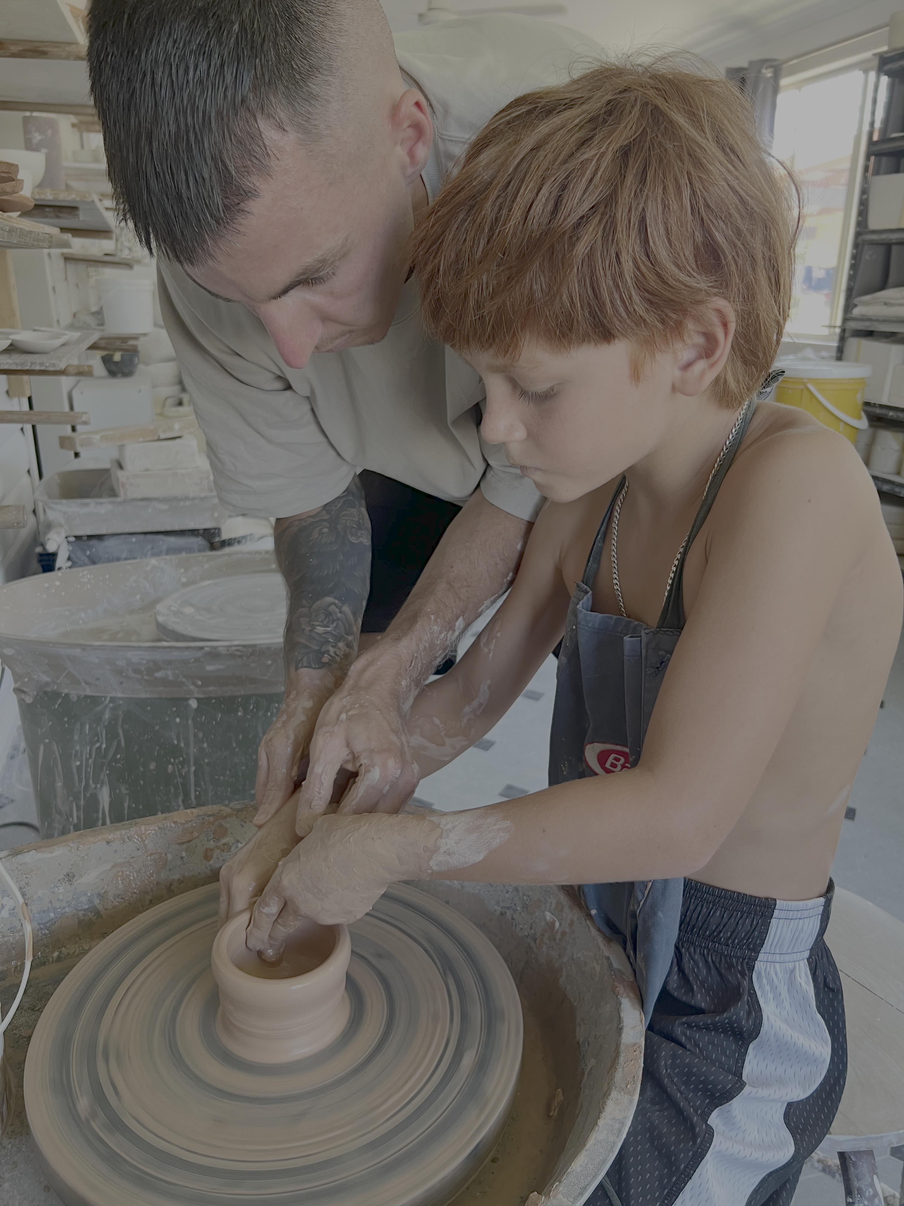Migs and Riley shaping a pot together at the pottery wheel